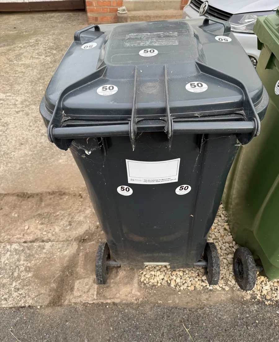 Black rubbish bin with several round address stickers on the lid and front